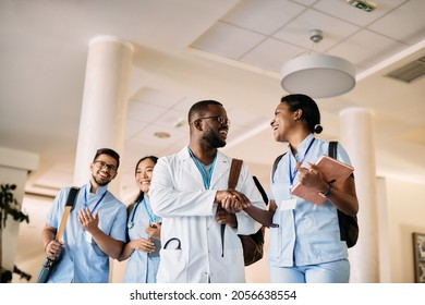 Low angle view of African American medical student shaking hands with female colleagues at medical university hallway.  - Powered by Shutterstock