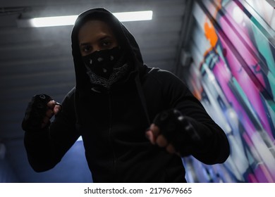 Low angle view of african american bandit in mask standing in fighting pose near graffiti in garage - Shutterstock ID 2179679665