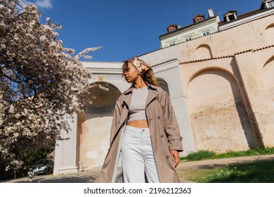 Low Angle View Of African American Woman In Trendy Outfit Standing Near Blooming Tree In Prague