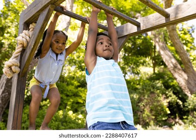 Low angle view of african american sister and brother hanging on monkeys bars at playground. Unaltered, family, togetherness, childhood, playing, enjoyment and weekend concept. - Powered by Shutterstock