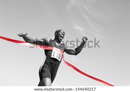 Low angle view of an African American male runner crossing finish line against blue sky