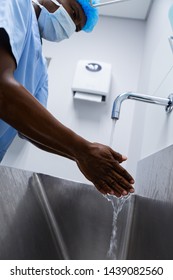 Low angle view of African-american male surgeon washing hands in sink at hospital, Coronavirus hand washing for clean hands hygiene Covid19 spread prevention.
