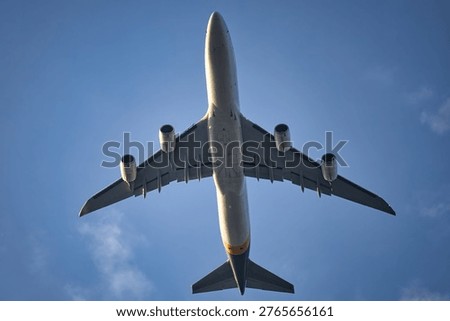 Low angle view of a airplane flying overhead against a clear blue sky with sparse clouds, highlighting underside details and powerful engines in bright daylight.