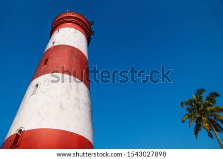 Low angle view of Alleppey Lighthouse with red and white stripes with palm tree on cloudless blue sky, Aleppuzha, Kerala, India