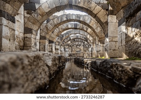 Low angle view of ancient Roman arches reflected in a water canal within the Agora of Smyrna, Izmir, Turkey. Historic stone masonry and architecture of an antique open-air museum.