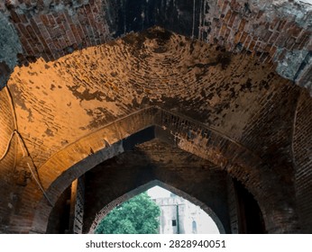 Low angle view of an ancient vaulted brick ceiling and pointed arches inside a historic Mughal gateway.
