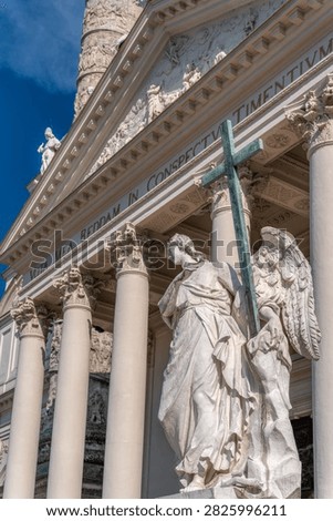 Low angle view of angel statue holding a cross with Karlskirche portico and columns in background in Vienna