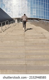 Low Angle View Of Anonymous Black Male Athlete Running Up Concrete Steps Towards Contemporary Office Building While Having Outdoor Workout