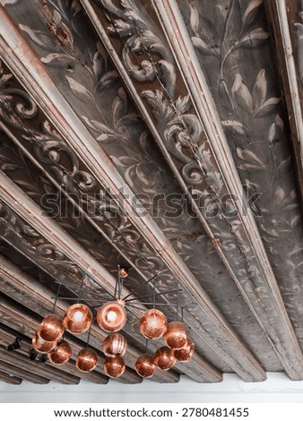Low angle view of an antique painted wooden beam ceiling with floral patterns and a modern copper chandelier