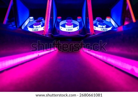 Low angle view of an arcade skee-ball lane illuminated with bright purple and blue neon lights, creating a vibrant gaming and nightlife atmosphere.