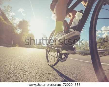 Low angle view of an athlete pushing on the pedals of a racing bicycle during a sport competition. Backlit shot with lens flare.