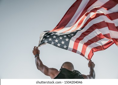 Low angle view of an athlete running on athletic track holding the american flag over the head - Powered by Shutterstock