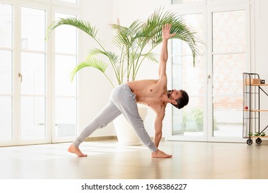 Low angle view of an athletic man doing a Parivrtta trikonasana or Triangle yoga pose stretching and strengthening his core muscles in a high key gym with copyspace in a health and fitness concept