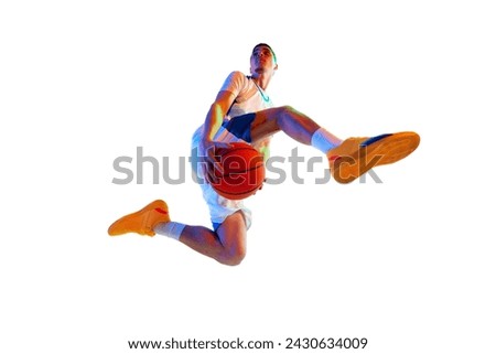 Low angle view. Athletic man in mid-jump shot with basketball ball against white studio background in neon light. Concept of professional sport, energy, strength and power, championship, tournament.