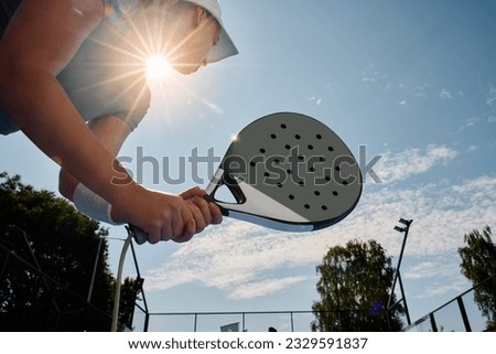 Low angle view of athletic woman playing paddle tennis on outdoor court. 