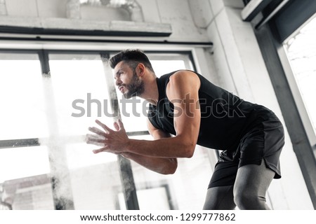 low angle view of athletic young man applying talcum powder on hands and looking away in gym