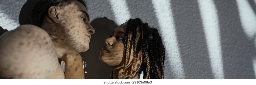 low angle view of attractive and seductive african american woman with stylish dreadlocks standing near sexy shirtless man on white textured background with grey shadows, banner