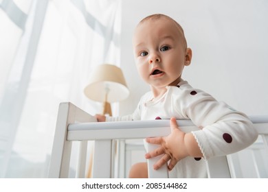 Low Angle View Of Baby Boy Looking At Camera From Crib At Home