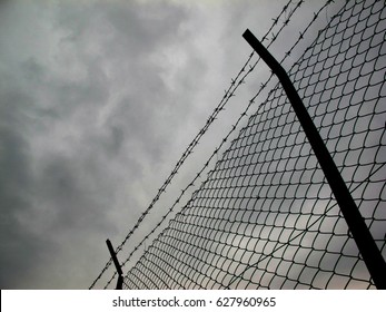 Low angle view of barbed wire and chain link fence against cloudy sky - Shutterstock ID 627960965