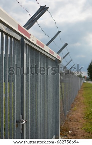 Low angle view of barbed wire and chain link fence against cloudy sky