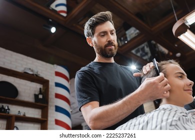 Low Angle View Of Barber Combing Hair Of Teen Client In Barbershop