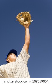 Low Angle View Of Baseball Player Trying To Catch The Ball Against Blue Sky