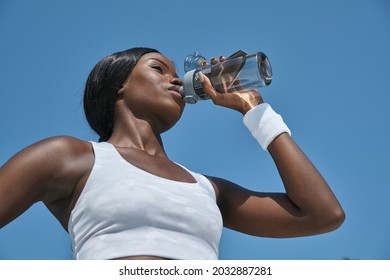 Low angle view of beautiful young African woman in sports clothing drinking water - Shutterstock ID 2032887281