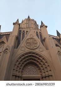 
A low angle view of a beige gothic style building with intricate rose window, pointed arches, and tall spires against a clear pale blue sky, showing detailed architectural design and majestic atmosphere.  
