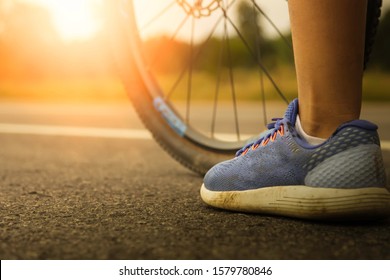 A low angle view of a bicycle's front wheel with a backdrop of green trees and orange lights of the sun in the evening, cyclists like to ride bicycles on the weekends to exercise to health.