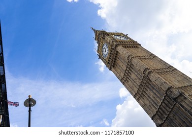 Low angle view of the Big Ben in London England United Kingdom against a blue sky with white clouds and a Union Jack British flag on a building and a streetlight