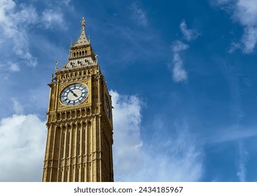 A low angle view of Big Ben against a blue sky with some white clouds in Westminster, London, England.