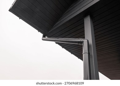 Low angle view of black rain gutter system on wooden roof soffit