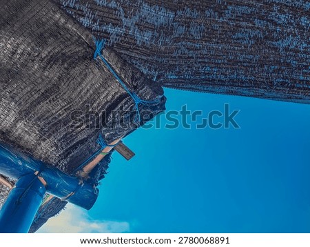Low angle view of black shade net structure against a clear blue sky, secured with blue ropes on a bamboo pole