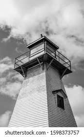 A Low Angle View, Black And White Photo Of A Classic, 19th Century Wooden Lighthouse Under Large Storm Clouds.