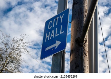 Low Angle View Of A Blue City Hall Directional Sign, Pointing The Direction Of A Local City's Government Building In The Pacific Northwest On A Cloudy Day