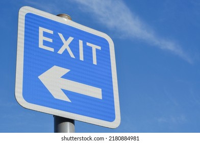 Low angle view of blue and white EXIT road sign with directional arrow symbol pointing to the left hand side, against a bright blue sky background. - Shutterstock ID 2180884981