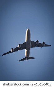 Low angle view of a Boeing 747 flying overhead against a clear blue sky with sparse clouds, highlighting underside details and powerful engines in bright daylight.