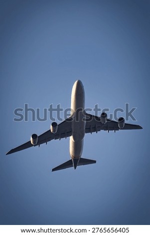 Low angle view of a Boeing 747 flying overhead against a clear blue sky with sparse clouds, highlighting underside details and powerful engines in bright daylight.