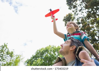 Low angle view of a boy with toy aeroplane sitting on father's shoulders at the park - Powered by Shutterstock