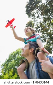 Low angle view of a boy with toy aeroplane sitting on father's shoulders at the park