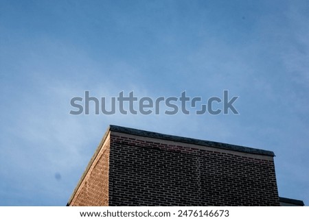 Low angle view of a brick building corner against a clear blue sky; minimalist architecture.