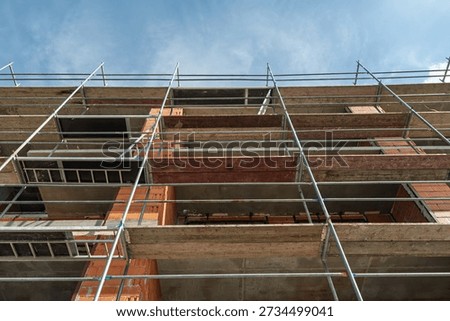 Low angle view of brick building renovation with metal scaffolding and wooden planks under blue sky, concept of construction work.