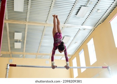 Low angle view at brunette female gymnast dressed in purple leotard pausing in handstand at top of uneven bars, copy space - Powered by Shutterstock