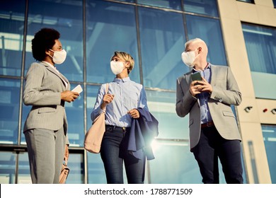 Low Angle View Of Business Coworkers With Protective Face Masks Talking While Standing In Front Of Their Office Building. 