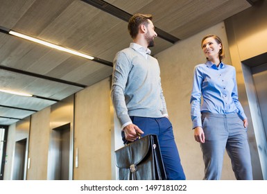 Low Angle View Of Business People Talking While Walking Against Elevator In Office