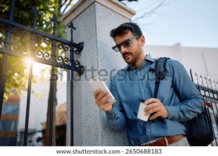 Low angle view of businessman using mobile phone on his way to work. 