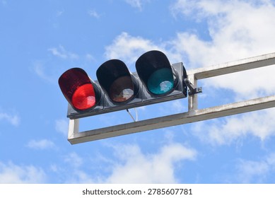 A low angle view captures a horizontal three-lens traffic light showing a bright red signal mounted on a steel structure under a cloudy blue sky.