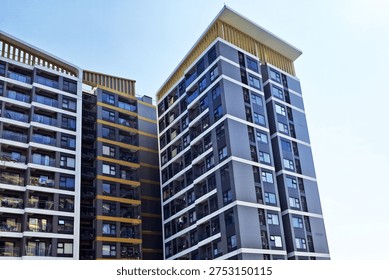 Low angle view capturing multiple modern residential high rise buildings featuring dark grey and yellow accents against a bright, clear sky, ideal for real estate concepts.