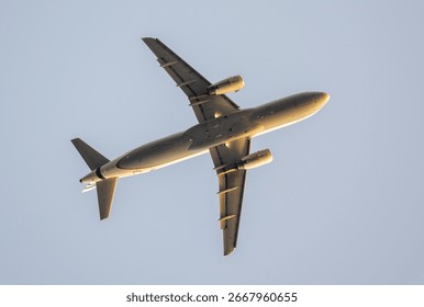 Low angle view capturing passenger airplane soaring against clear blue sky, revealing aircraft underside details and wing configuration