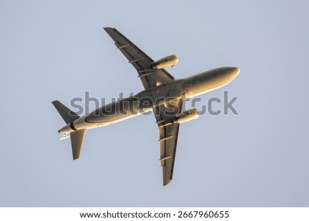 Low angle view capturing passenger airplane soaring against clear blue sky, revealing aircraft underside details and wing configuration